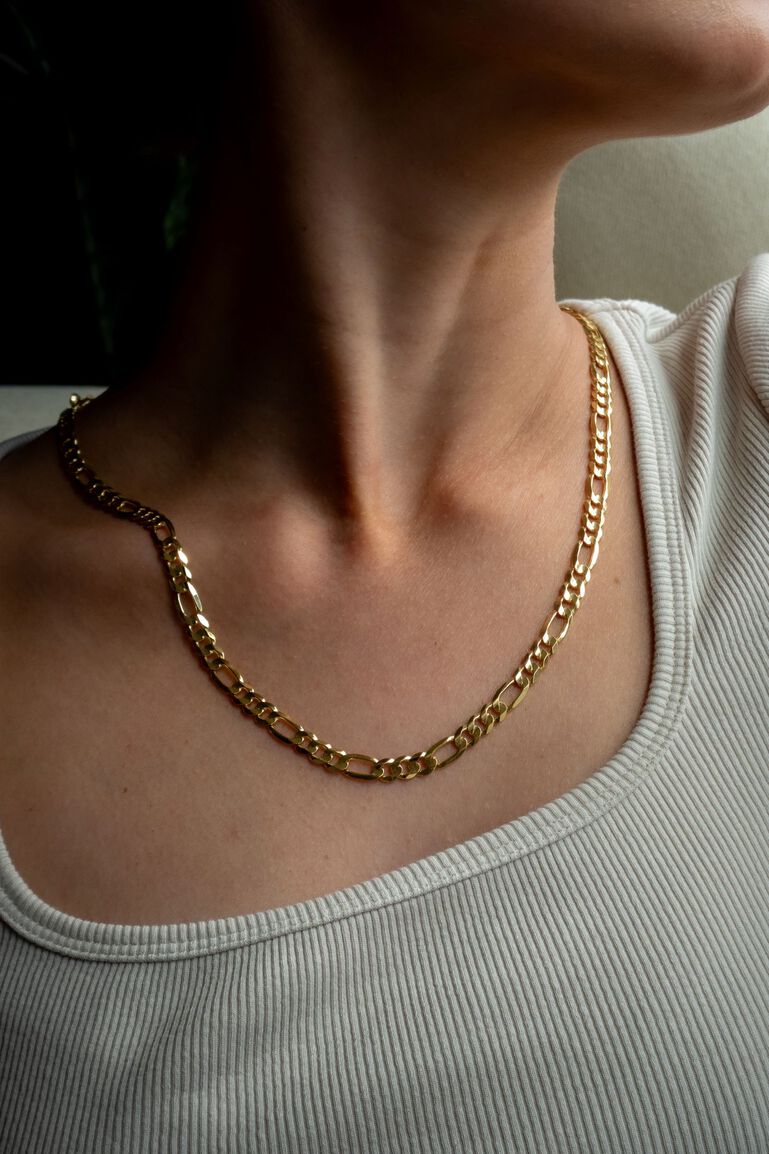 A Figaro chain in yellow gold reflects the light while being worn on a woman's neck. 